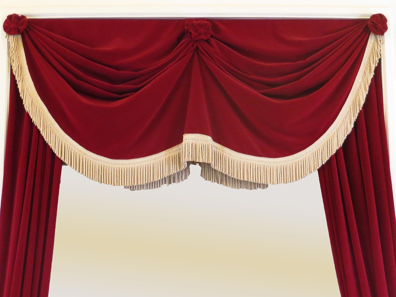 Un rideau de theatre en velours rouge vu de face, drape en festons et retenu en trois points par des embrasses, borde d'une frange creme, s'ouvrant sur un fond clair et vide: ni scene ni salle ne sont visibles