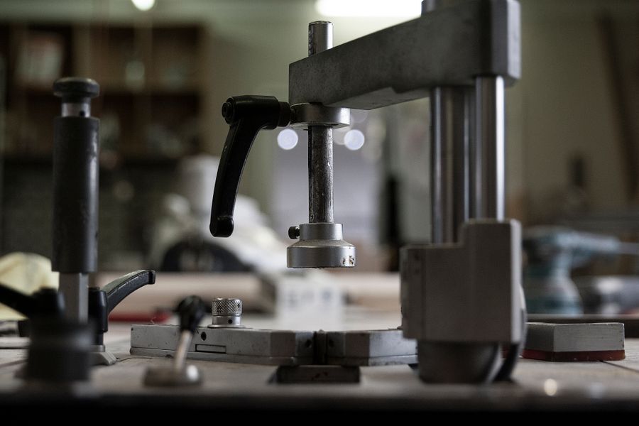 Une perceuse a colonne d'etabli en gros plan dans un atelier, levier noir en premier plan, etageres floues a l'arriere-plan